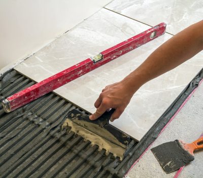 Ceramic tiles and tools for tiler. Worker hand installing floor tiles. Home improvement, renovation