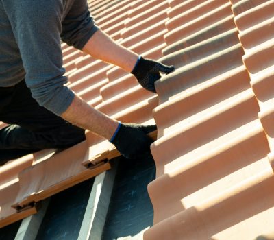 Closeup of worker hands installing yellow ceramic roofing tiles mounted on wooden boards covering