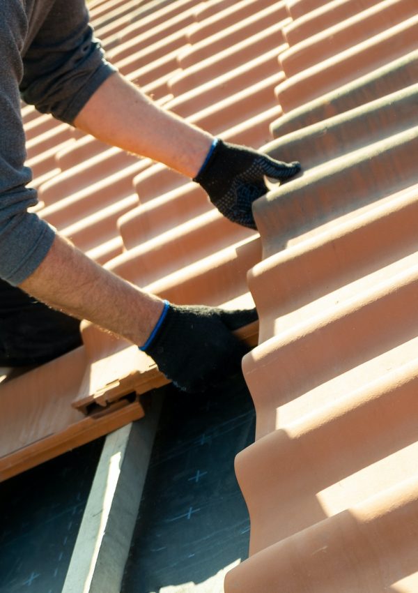Closeup of worker hands installing yellow ceramic roofing tiles mounted on wooden boards covering